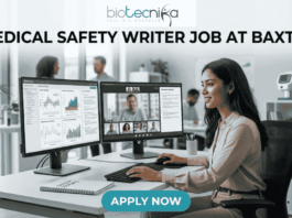 Medical Safety Writer Job at Baxter – High Demand Life Science Role in Ahmedabad! A sleek, realistic featured image for a career opportunity. The Biotecnika logo is at the top. The bold heading "MEDICAL SAFETY WRITER JOB AT BAXTER" spans the upper section. The image depicts a female professional sitting at a clean, modern desk with dual monitors; one screen shows data charts and the other shows a video conference with colleagues. The setting is a bright, contemporary office with a DNA model in the background. A blue and teal gradient "APPLY NOW" button is located at the bottom center.