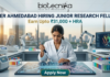NIPER Ahmedabad Hiring Junior Research Fellow Earn Upto ₹31,000 + HRA Apply Fast! A professional featured image for a Junior Research Fellow (JRF) job opening at NIPER Ahmedabad, created for Biotecnika. The scene features a female scientist in a white lab coat using a pipette over a glowing, futuristic digital workbench displaying molecular structures. The laboratory is equipped with advanced technology, including robotic arms and high-end centrifuges, with a modern city skyline visible through large windows in the background. The bold heading "NIPER AHMEDABAD HIRING JUNIOR RESEARCH FELLOW" and the tagline "Earn Upto ₹31,000 + HRA" are prominently displayed, with an "Apply Now" button at the bottom.