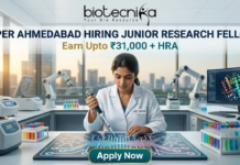 NIPER Ahmedabad Hiring Junior Research Fellow | Earn Upto ₹31,000 + HRA | Apply Fast! NIPER Ahmedabad Hiring Junior Research Fellow Earn Upto ₹31,000 + HRA Apply Fast! A professional featured image for a Junior Research Fellow (JRF) job opening at NIPER Ahmedabad, created for Biotecnika. The scene features a female scientist in a white lab coat using a pipette over a glowing, futuristic digital workbench displaying molecular structures. The laboratory is equipped with advanced technology, including robotic arms and high-end centrifuges, with a modern city skyline visible through large windows in the background. The bold heading "NIPER AHMEDABAD HIRING JUNIOR RESEARCH FELLOW" and the tagline "Earn Upto ₹31,000 + HRA" are prominently displayed, with an "Apply Now" button at the bottom.