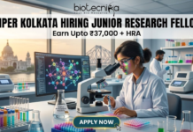 NIPER Kolkata Hiring Junior Research Fellow | Get Upto ₹37,000 + HRA | Apply Online Now!! NIPER Kolkata Hiring Junior Research Fellow. Alt Text: A high-quality, professional featured image for a "Junior Research Fellow" job opening at NIPER Kolkata. The scene features a focused female scientist in a white lab coat and safety glasses working in a futuristic laboratory. Through the large windows, iconic Kolkata landmarks like the Victoria Memorial and the Howrah Bridge are visible at sunset. The image includes the Biotecnika logo at the top center, the bold headline "NIPER KOLKATA HIRING JUNIOR RESEARCH FELLOW," and a tagline stating "Earn Upto ₹37,000 + HRA." A prominent "APPLY NOW" button is positioned at the bottom center.