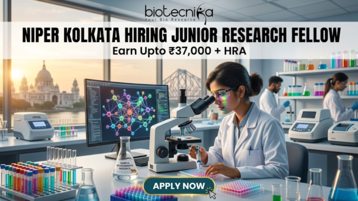 NIPER Kolkata Hiring Junior Research Fellow. Alt Text: A high-quality, professional featured image for a "Junior Research Fellow" job opening at NIPER Kolkata. The scene features a focused female scientist in a white lab coat and safety glasses working in a futuristic laboratory. Through the large windows, iconic Kolkata landmarks like the Victoria Memorial and the Howrah Bridge are visible at sunset. The image includes the Biotecnika logo at the top center, the bold headline "NIPER KOLKATA HIRING JUNIOR RESEARCH FELLOW," and a tagline stating "Earn Upto ₹37,000 + HRA." A prominent "APPLY NOW" button is positioned at the bottom center.
