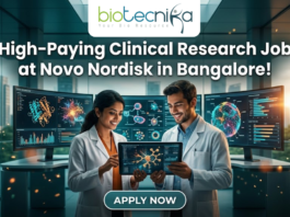 Novo Nordisk Hiring Clinical Data Scientist – High-Paying Clinical Research Job in Bangalore! Novo Nordisk Hiring Clinical Data Scientist – High-Paying Clinical Research Job in Bangalore! A promotional featured image for a job opening, featuring the headline "High-Paying Clinical Research Job at Novo Nordisk in Bangalore!" in bold white text at the top. The Biotecnika logo is positioned at the top center. The central visual shows two professional researchers—a woman and a man in white lab coats—smiling and collaborating while looking at a digital tablet that displays a glowing neural network. They are standing in a futuristic, high-tech laboratory equipped with large, curved monitors showing 3D protein structures and complex biological data. Through the large glass windows behind them, a modern city skyline is visible during a warm sunset. At the bottom center, there is a prominent, stylized "APPLY NOW" button.