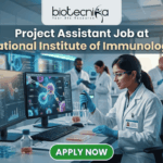Project Assistant Job at National Institute of Immunology – Apply for Life Science Research Role Now! A promotional graphic for "biotecnika Your Bio Resource," set in a modern, busy laboratory environment. At the top center, the text "biotecnika Your Bio Resource" is displayed. Below it, the large headline "Project Assistant Job at National Institute of Immunology" is prominently featured in a white, sans-serif font. The main image shows a woman in a white lab coat, glasses, and blue gloves, using a pipette at a desk with dual computer monitors displaying complex molecular structures and scientific data. Other researchers work in the background. A large green button at the bottom contains the text "APPLY NOW". Various lab equipment is visible, and the overall color scheme is in blues, greens, white, and gold.