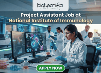 Project Assistant Job at National Institute of Immunology – Apply for Life Science Research Role Now! Project Assistant Job at National Institute of Immunology – Apply for Life Science Research Role Now! A promotional graphic for "biotecnika Your Bio Resource," set in a modern, busy laboratory environment. At the top center, the text "biotecnika Your Bio Resource" is displayed. Below it, the large headline "Project Assistant Job at National Institute of Immunology" is prominently featured in a white, sans-serif font. The main image shows a woman in a white lab coat, glasses, and blue gloves, using a pipette at a desk with dual computer monitors displaying complex molecular structures and scientific data. Other researchers work in the background. A large green button at the bottom contains the text "APPLY NOW". Various lab equipment is visible, and the overall color scheme is in blues, greens, white, and gold.
