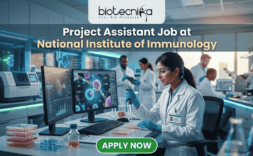 Project Assistant Job at National Institute of Immunology – Apply for Life Science Research Role Now! Project Assistant Job at National Institute of Immunology – Apply for Life Science Research Role Now! A promotional graphic for "biotecnika Your Bio Resource," set in a modern, busy laboratory environment. At the top center, the text "biotecnika Your Bio Resource" is displayed. Below it, the large headline "Project Assistant Job at National Institute of Immunology" is prominently featured in a white, sans-serif font. The main image shows a woman in a white lab coat, glasses, and blue gloves, using a pipette at a desk with dual computer monitors displaying complex molecular structures and scientific data. Other researchers work in the background. A large green button at the bottom contains the text "APPLY NOW". Various lab equipment is visible, and the overall color scheme is in blues, greens, white, and gold.
