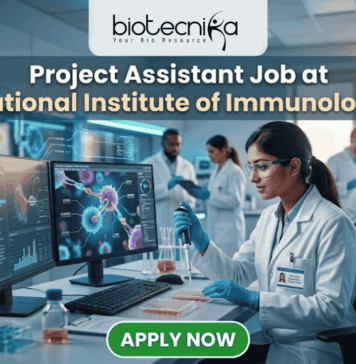 Project Assistant Job at National Institute of Immunology – Apply for Life Science Research Role Now! Project Assistant Job at National Institute of Immunology – Apply for Life Science Research Role Now! A promotional graphic for "biotecnika Your Bio Resource," set in a modern, busy laboratory environment. At the top center, the text "biotecnika Your Bio Resource" is displayed. Below it, the large headline "Project Assistant Job at National Institute of Immunology" is prominently featured in a white, sans-serif font. The main image shows a woman in a white lab coat, glasses, and blue gloves, using a pipette at a desk with dual computer monitors displaying complex molecular structures and scientific data. Other researchers work in the background. A large green button at the bottom contains the text "APPLY NOW". Various lab equipment is visible, and the overall color scheme is in blues, greens, white, and gold.