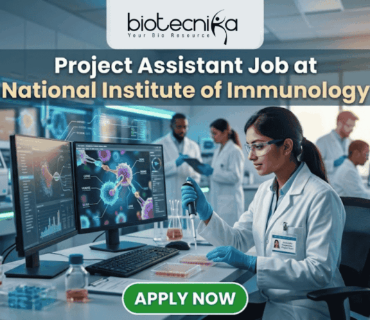 Project Assistant Job at National Institute of Immunology – Apply for Life Science Research Role Now! A promotional graphic for "biotecnika Your Bio Resource," set in a modern, busy laboratory environment. At the top center, the text "biotecnika Your Bio Resource" is displayed. Below it, the large headline "Project Assistant Job at National Institute of Immunology" is prominently featured in a white, sans-serif font. The main image shows a woman in a white lab coat, glasses, and blue gloves, using a pipette at a desk with dual computer monitors displaying complex molecular structures and scientific data. Other researchers work in the background. A large green button at the bottom contains the text "APPLY NOW". Various lab equipment is visible, and the overall color scheme is in blues, greens, white, and gold.