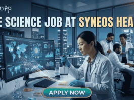 Top Life Science Job at Syneos Health – Central Monitor Role Hiring Now! Life Science Job at Syneos Health | Central Monitor Role. A professional promotional graphic for a "Life Science Job at Syneos Health" featuring the Biotecnika logo at the top. The image depicts a female scientist in a white lab coat and blue gloves using a multichannel pipette on a microplate in a modern, high-tech laboratory. A large computer monitor in the foreground displays complex global data visualizations, including a world map with interconnected nodes, cellular diagrams, and data graphs. In the background, other researchers are seen working at their stations. The laboratory features large glass windows that reveal a glowing city skyline at night. A large, prominent "APPLY NOW" button is centered at the bottom.