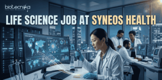 Top Life Science Job at Syneos Health – Central Monitor Role Hiring Now! Life Science Job at Syneos Health | Central Monitor Role. A professional promotional graphic for a "Life Science Job at Syneos Health" featuring the Biotecnika logo at the top. The image depicts a female scientist in a white lab coat and blue gloves using a multichannel pipette on a microplate in a modern, high-tech laboratory. A large computer monitor in the foreground displays complex global data visualizations, including a world map with interconnected nodes, cellular diagrams, and data graphs. In the background, other researchers are seen working at their stations. The laboratory features large glass windows that reveal a glowing city skyline at night. A large, prominent "APPLY NOW" button is centered at the bottom.