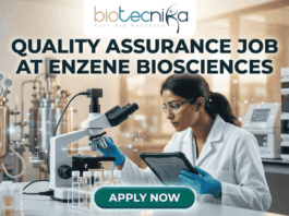 Latest Quality Assurance Job at Enzene Biosciences | Biotechnology & Microbiology Candidates Apply Now A professional promotional graphic for a Quality Assurance Job at Enzene Biosciences. At the top center is the Biotecnika Professional logo, followed by the headline "QUALITY ASSURANCE JOB AT ENZENE BIOSCIENCES" in bold, dark green lettering. The image features a female scientist in a white lab coat and safety glasses, focused on a digital tablet while working in a high-tech laboratory. The setting includes a microscope, rows of clear vials on a lab bench, and large-scale industrial bioreactors in the background. A glowing teal "APPLY NOW" button is positioned prominently at the bottom center.