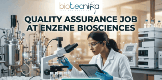 Latest Quality Assurance Job at Enzene Biosciences | Biotechnology & Microbiology Candidates Apply Now A professional promotional graphic for a Quality Assurance Job at Enzene Biosciences. At the top center is the Biotecnika Professional logo, followed by the headline "QUALITY ASSURANCE JOB AT ENZENE BIOSCIENCES" in bold, dark green lettering. The image features a female scientist in a white lab coat and safety glasses, focused on a digital tablet while working in a high-tech laboratory. The setting includes a microscope, rows of clear vials on a lab bench, and large-scale industrial bioreactors in the background. A glowing teal "APPLY NOW" button is positioned prominently at the bottom center.