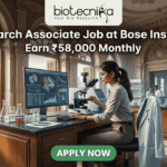 Research Associate Job at Bose Institute – Earn ₹58,000 Monthly in Top Life Science Project! A professional featured image for a job posting titled "Research Associate Job at Bose Institute" with a tagline "Earn ₹58,000 Monthly." The image depicts a female scientist in a white lab coat and glasses working with a microscope and a computer monitor displaying complex molecular structures. The setting is a majestic, classical laboratory with high arched windows and ornate architecture. Visible through the window is a scenic view of Kolkata, featuring a signature yellow taxi and a river with traditional boats. The Biotecnika logo is positioned at the top, and a prominent green "APPLY NOW" button is located at the bottom center.
