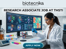 Research Associate Job at THSTI PhD Life Sciences Candidates Earn Upto ₹47,000. A realistic, high-tech featured image for a "Research Associate Job at THSTI." At the top is the Biotecnika logo. The center features a female scientist in a white lab coat and safety glasses, meticulously using a pipette over a multi-well plate. Behind her, a large curved monitor displays complex molecular structures and colorful genomic data charts. The modern laboratory is filled with advanced scientific equipment like a bioreactor and centrifuge. At the bottom, there is a prominent teal "APPLY NOW" button.