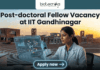 Research Associate Opportunity at IIT Gandhinaga. A featured image with a prominent heading that reads: 'Post-doctoral Fellow Vacancy at IIT Gandhinagar'. The image is divided, showing a modern university campus on the left and a female scientist in a lab coat on the right, pipetting a sample into a multi-well plate. She is interacting with a futuristic, holographic data display. The 'biotecnika Global' logo is at the top center, and a large green 'Apply now' button with an arrow is at the bottom center. The overall style is a clean, professional composite photograph.