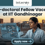 Research Associate Opportunity at IIT Gandhinaga. A featured image with a prominent heading that reads: 'Post-doctoral Fellow Vacancy at IIT Gandhinagar'. The image is divided, showing a modern university campus on the left and a female scientist in a lab coat on the right, pipetting a sample into a multi-well plate. She is interacting with a futuristic, holographic data display. The 'biotecnika Global' logo is at the top center, and a large green 'Apply now' button with an arrow is at the bottom center. The overall style is a clean, professional composite photograph.