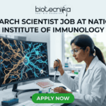 Research Scientist Job at National Institute of Immunology – Cancer Biology Project Hiring Now! "A featured image job banner titled 'RESEARCH SCIENTIST JOB AT NATIONAL INSTITUTE OF IMMUNOLOGY' and featuring the biotecnika 'IMMUNOLOG TECH' logo, depicting a focused Indian female scientist in a lab coat using a pipette while a complex, multi-colored 3D map of immune cell pathways is displayed on her curved monitor, with other high-tech lab equipment in the blurred background and a green 'APPLY NOW' button at the bottom."