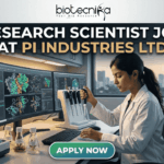 Research Scientist Role in Molecular Biology at PI Industries Ltd – Apply Now! Research Scientist Job at PI Industries Ltd Hyderabad Apply Now. A featured image graphic for a biotechnology research scientist job listing. At the top, the biotecnika "Your Bio Resource" logo is displayed. Below, large bold text in white and gold reads "RESEARCH SCIENTIST JOB AT PI INDUSTRIES LTD". The central image is a realistic photograph of a focused young female Indian scientist in a lab coat, operating a multi-channel pipette station. Her curved multi-monitor setup displays stunning, unique multi-color molecular pathway and docking visualizations. The modern research lab around her includes advanced equipment, tissue cultures, and unique labeled plant samples. Through a large window in the background, a view of an Indian city skyline (like Bengaluru or Ahmedabad) during a warm sunset creates a relatable, scroll-stopping setting. At the bottom center, a rounded gradient green-to-blue "APPLY NOW" button provides a clear call to action. The entire composition is realistic and visually attractive.