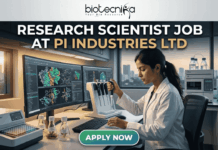 Research Scientist Role in Molecular Biology at PI Industries Ltd – Apply Now! Research Scientist Job at PI Industries Ltd Hyderabad Apply Now. A featured image graphic for a biotechnology research scientist job listing. At the top, the biotecnika "Your Bio Resource" logo is displayed. Below, large bold text in white and gold reads "RESEARCH SCIENTIST JOB AT PI INDUSTRIES LTD". The central image is a realistic photograph of a focused young female Indian scientist in a lab coat, operating a multi-channel pipette station. Her curved multi-monitor setup displays stunning, unique multi-color molecular pathway and docking visualizations. The modern research lab around her includes advanced equipment, tissue cultures, and unique labeled plant samples. Through a large window in the background, a view of an Indian city skyline (like Bengaluru or Ahmedabad) during a warm sunset creates a relatable, scroll-stopping setting. At the bottom center, a rounded gradient green-to-blue "APPLY NOW" button provides a clear call to action. The entire composition is realistic and visually attractive.
