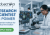 Research Scientist Vacancy at PGIMER Earn Upto ₹56,000. A featured image for a job page with a clean, professional layout. On the left side, against a light blue and white background, the Biotecnika logo is at the top, followed by the bold blue text "RESEARCH SCIENTIST at PGIMER" and a tagline "A Premier Institute for Medical Innovation." At the bottom left is a green "APPLY NOW" button. The right side of the image features a realistic, high-quality photo of a female scientist in a white lab coat and safety glasses working with a pipette in a modern laboratory. In the background, large computer monitors display vibrant, detailed microscopic imaging of cell structures.
