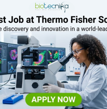Scientist Job at Thermo Fisher Scientific – High-Paying R&D Role in Bangalore! Scientist Job at Thermo Fisher Scientific | High-Paying R&D Role. A professional featured image for a "Scientist Job at Thermo Fisher Scientific." The visual shows a female scientist in a white lab coat, smiling and working with a microscope in a high-tech laboratory. In the background, large computer monitors display colorful, high-resolution cellular imaging. The Biotecnika logo is positioned at the top, and a prominent green "APPLY NOW" button is at the bottom center.