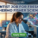Scientist Job for Freshers at Thermo Fisher Scientific Apply Now. A recruitment advertisement image shows a female scientist in a lab coat smiling while looking into a microscope, from which a complex, colorful holographic neural network projection emerges. Overlaid text at the top reads, "SCIENTIST JOB FOR FRESHERS AT THERMO FISHER SCIENTIFIC" with the "biotecnika" logo above it. A green "Apply Now" button is at the bottom center.