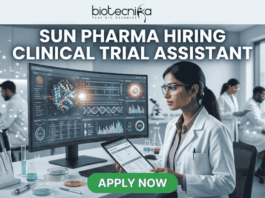 Sun Pharma Hiring Clinical Trial Assistant Apply Now. A professional and high-tech promotional image for a job opening. At the top, the Biotecnika logo is placed above the bold, capitalized headline: "SUN PHARMA HIRING CLINICAL TRIAL ASSISTANT". The central focus is a female scientist in a white lab coat and safety glasses, intently working at a desk. She is looking at a large, curved digital monitor that displays intricate clinical trial data, 3D molecular structures, and a glowing sun-like graphic representing the company theme. The laboratory setting is bright and modern, with other researchers working in the background and scientific equipment like pipettes and vials visible on the desk. At the bottom center, a vibrant green "APPLY NOW" button stands out, making the image an effective, scroll-stopping recruitment graphic.