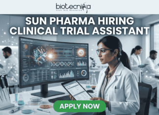 Sun Pharma Hiring Clinical Trial Assistant | Apply for Clinical Research Job! Sun Pharma Hiring Clinical Trial Assistant Apply Now. A professional and high-tech promotional image for a job opening. At the top, the Biotecnika logo is placed above the bold, capitalized headline: "SUN PHARMA HIRING CLINICAL TRIAL ASSISTANT". The central focus is a female scientist in a white lab coat and safety glasses, intently working at a desk. She is looking at a large, curved digital monitor that displays intricate clinical trial data, 3D molecular structures, and a glowing sun-like graphic representing the company theme. The laboratory setting is bright and modern, with other researchers working in the background and scientific equipment like pipettes and vials visible on the desk. At the bottom center, a vibrant green "APPLY NOW" button stands out, making the image an effective, scroll-stopping recruitment graphic.