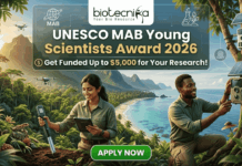 UNESCO MAB Young Scientists Award 2026 – Get Funded Up to $5,000 for Your Research! A featured job post image for the UNESCO MAB Young Scientists Award 2026. At the top center is the Biotecnika logo. The main text reads "UNESCO MAB Young Scientists Award 2026" with a sub-headline, "Get Funded Up to $5,000 for Your Research!" The background features a realistic and vibrant tropical coastal landscape with lush green mountains and turquoise water. Two scientists—a woman and a man in khaki field gear—are shown conducting environmental research; the woman uses a handheld probe and tablet while the man inspects a sensor device mounted on a tree. Drones fly in the background, emphasizing a high-tech conservation theme. At the bottom center is a prominent green "APPLY NOW" button.