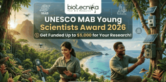 UNESCO MAB Young Scientists Award 2026 – Get Funded Up to $5,000 for Your Research! A featured job post image for the UNESCO MAB Young Scientists Award 2026. At the top center is the Biotecnika logo. The main text reads "UNESCO MAB Young Scientists Award 2026" with a sub-headline, "Get Funded Up to $5,000 for Your Research!" The background features a realistic and vibrant tropical coastal landscape with lush green mountains and turquoise water. Two scientists—a woman and a man in khaki field gear—are shown conducting environmental research; the woman uses a handheld probe and tablet while the man inspects a sensor device mounted on a tree. Drones fly in the background, emphasizing a high-tech conservation theme. At the bottom center is a prominent green "APPLY NOW" button.
