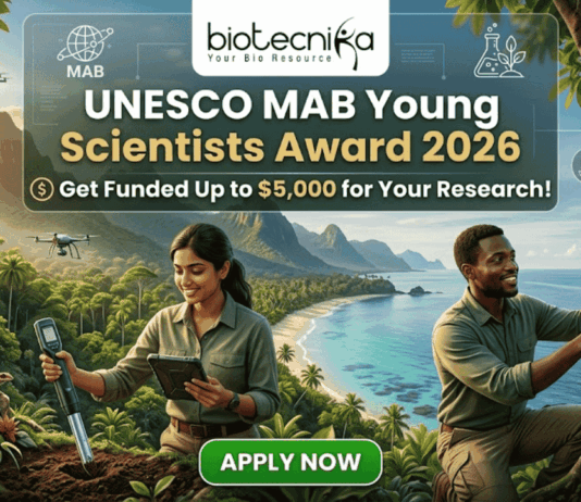 UNESCO MAB Young Scientists Award 2026 – Get Funded Up to $5,000 for Your Research! A featured job post image for the UNESCO MAB Young Scientists Award 2026. At the top center is the Biotecnika logo. The main text reads "UNESCO MAB Young Scientists Award 2026" with a sub-headline, "Get Funded Up to $5,000 for Your Research!" The background features a realistic and vibrant tropical coastal landscape with lush green mountains and turquoise water. Two scientists—a woman and a man in khaki field gear—are shown conducting environmental research; the woman uses a handheld probe and tablet while the man inspects a sensor device mounted on a tree. Drones fly in the background, emphasizing a high-tech conservation theme. At the bottom center is a prominent green "APPLY NOW" button.
