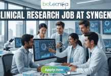 Urgent Hiring! Clinical Research Job at Syngene – Apply Today! Urgent Hiring! Clinical Research Job at Syngene – Apply Today! A featured image for a job page, part of Biotecnika, showcasing a clinical research position at Syngene. At the top center is the Biotecnika logo, with the text 'Your Bio Resource'. The main bold title is 'CLINICAL RESEARCH JOB AT SYNGENE'. The background features a detailed, realistic photograph of a diverse team of five scientists and professionals (two women, three men) collaborating in a modern, well-equipped laboratory, looking collaboratively into a computer monitor showing data charts, graphs, and a detailed 3D molecular structure. The lab has advanced scientific instruments, beakers, and shelves, visible next to a large window. The overall scene conveys scientific innovation, teamwork, and professionalism. At the bottom center, there is a prominent orange rectangular button labeled 'Apply now'.