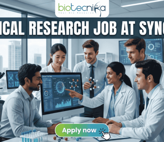 Urgent Hiring! Clinical Research Job at Syngene – Apply Today! A featured image for a job page, part of Biotecnika, showcasing a clinical research position at Syngene. At the top center is the Biotecnika logo, with the text 'Your Bio Resource'. The main bold title is 'CLINICAL RESEARCH JOB AT SYNGENE'. The background features a detailed, realistic photograph of a diverse team of five scientists and professionals (two women, three men) collaborating in a modern, well-equipped laboratory, looking collaboratively into a computer monitor showing data charts, graphs, and a detailed 3D molecular structure. The lab has advanced scientific instruments, beakers, and shelves, visible next to a large window. The overall scene conveys scientific innovation, teamwork, and professionalism. At the bottom center, there is a prominent orange rectangular button labeled 'Apply now'.