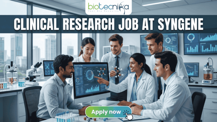 Urgent Hiring! Clinical Research Job at Syngene – Apply Today! Urgent Hiring! Clinical Research Job at Syngene – Apply Today! A featured image for a job page, part of Biotecnika, showcasing a clinical research position at Syngene. At the top center is the Biotecnika logo, with the text 'Your Bio Resource'. The main bold title is 'CLINICAL RESEARCH JOB AT SYNGENE'. The background features a detailed, realistic photograph of a diverse team of five scientists and professionals (two women, three men) collaborating in a modern, well-equipped laboratory, looking collaboratively into a computer monitor showing data charts, graphs, and a detailed 3D molecular structure. The lab has advanced scientific instruments, beakers, and shelves, visible next to a large window. The overall scene conveys scientific innovation, teamwork, and professionalism. At the bottom center, there is a prominent orange rectangular button labeled 'Apply now'.