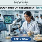 Freshers Hiring! Quality Executive Job at iD Fresh Food | Microbiology & Food Tech Eligible iD Fresh Food Hiring Quality Executive for Microbiology Job Freshers Eligible. A professional and high-quality featured image advertisement for a "Microbiology Job for Freshers at iD Fresh Food." The scene depicts a female scientist in a white lab coat and safety goggles working in a modern, high-tech Food Safety & Quality Lab. She is carefully testing food samples, such as idli/dosa batter and parottas, using a pipette and lab equipment. A computer monitor in the background shows detailed microbial cell structures. The Biotecnika logo is at the top center, the job title is displayed in bold black text, and a prominent blue "APPLY NOW" button is located at the bottom.