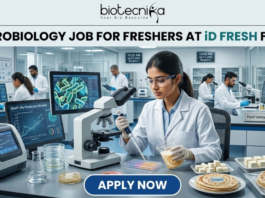 Freshers Hiring! Quality Executive Job at iD Fresh Food | Microbiology & Food Tech Eligible iD Fresh Food Hiring Quality Executive for Microbiology Job Freshers Eligible. A professional and high-quality featured image advertisement for a "Microbiology Job for Freshers at iD Fresh Food." The scene depicts a female scientist in a white lab coat and safety goggles working in a modern, high-tech Food Safety & Quality Lab. She is carefully testing food samples, such as idli/dosa batter and parottas, using a pipette and lab equipment. A computer monitor in the background shows detailed microbial cell structures. The Biotecnika logo is at the top center, the job title is displayed in bold black text, and a prominent blue "APPLY NOW" button is located at the bottom.