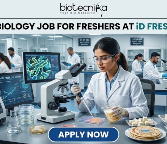 iD Fresh Food Hiring Quality Executive for Microbiology Job Freshers Eligible. A professional and high-quality featured image advertisement for a "Microbiology Job for Freshers at iD Fresh Food." The scene depicts a female scientist in a white lab coat and safety goggles working in a modern, high-tech Food Safety & Quality Lab. She is carefully testing food samples, such as idli/dosa batter and parottas, using a pipette and lab equipment. A computer monitor in the background shows detailed microbial cell structures. The Biotecnika logo is at the top center, the job title is displayed in bold black text, and a prominent blue "APPLY NOW" button is located at the bottom.