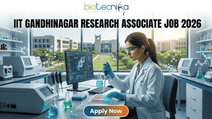 IIT Gandhinagar Research Associate Job 2026 – High Salary, Apply Before Deadline! A professional promotional image for a Research Associate job at IIT Gandhinagar in 2026. At the top, the Biotecnika Global logo is centered. Large, bold text reads "IIT GANDHINAGAR RESEARCH ASSOCIATE JOB 2026". In the center, a female scientist wearing a white lab coat and safety glasses is focused on her work, using a micropipette to dispense liquid into a multi-well plate. She sits in a modern, well-equipped laboratory with advanced research equipment and computer monitors displaying molecular data. Large windows in the background reveal a bright, green university campus. At the bottom, a prominent "Apply Now" button with an orange-to-green gradient is displayed.