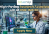 High-Paying Research Associate Job at CSIR-IMTECH – PhD Candidates Apply Now! Research Associate Job at CSIR-IMTECH | Apply Now. A high-quality promotional image for a "High-Paying Research Associate Job at CSIR-IMTECH" featuring the Biotecnika Global logo at the top center. The scene depicts a female scientist in a professional lab coat and safety goggles, carefully holding a flask filled with a glowing, bioluminescent green liquid. In the background, a modern laboratory is visible with a computer monitor displaying advanced microbial technology research, DNA structures, and molecular data. The lighting is a sleek, futuristic blue, and a prominent "Apply Now" button is positioned at the bottom center.