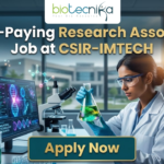 Research Associate Job at CSIR-IMTECH | Apply Now. A high-quality promotional image for a "High-Paying Research Associate Job at CSIR-IMTECH" featuring the Biotecnika Global logo at the top center. The scene depicts a female scientist in a professional lab coat and safety goggles, carefully holding a flask filled with a glowing, bioluminescent green liquid. In the background, a modern laboratory is visible with a computer monitor displaying advanced microbial technology research, DNA structures, and molecular data. The lighting is a sleek, futuristic blue, and a prominent "Apply Now" button is positioned at the bottom center.