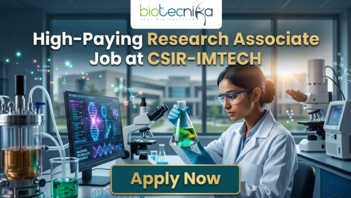 Research Associate Job at CSIR-IMTECH | Apply Now Research Associate Job at CSIR-IMTECH | Apply Now. A high-quality promotional image for a "High-Paying Research Associate Job at CSIR-IMTECH" featuring the Biotecnika Global logo at the top center. The scene depicts a female scientist in a professional lab coat and safety goggles, carefully holding a flask filled with a glowing, bioluminescent green liquid. In the background, a modern laboratory is visible with a computer monitor displaying advanced microbial technology research, DNA structures, and molecular data. The lighting is a sleek, futuristic blue, and a prominent "Apply Now" button is positioned at the bottom center.