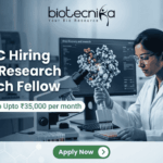 ACTREC Hiring Junior Research Fellow | Opportunity in Cancer Research ACTREC Hiring Junior Research Fellow Opportunity in Cancer Research. An advertisement for a Junior Research Fellow position at ACTREC, showing the Biotecnika logo at the top center. Text states: 'ACTREC Hiring Junior Research Fellow' and 'Get Fellowship Upto ₹35,000 per month'. A photograph on the right shows a female scientist in a lab coat, safety glasses, and blue gloves operating a multichannel pipette. Behind her, a monitor displays molecular drug discovery data. Various advanced lab instruments are in the background. At the bottom, a green 'Apply Now' button.