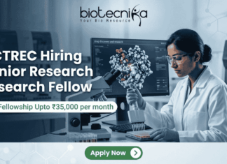 ACTREC Hiring Junior Research Fellow | Opportunity in Cancer Research ACTREC Hiring Junior Research Fellow Opportunity in Cancer Research. An advertisement for a Junior Research Fellow position at ACTREC, showing the Biotecnika logo at the top center. Text states: 'ACTREC Hiring Junior Research Fellow' and 'Get Fellowship Upto ₹35,000 per month'. A photograph on the right shows a female scientist in a lab coat, safety glasses, and blue gloves operating a multichannel pipette. Behind her, a monitor displays molecular drug discovery data. Various advanced lab instruments are in the background. At the bottom, a green 'Apply Now' button.
