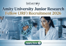 Amity University Junior Research Fellow (JRF) Recruitment 2026 | Apply Now Amity University Junior Research Fellow (JRF) Recruitment 2026 Apply Now. A featured image for a job posting titled "Amity University Junior Research Fellow (JRF) Recruitment 2026." At the top center is the Biotecnika logo. Below it, the main heading reads "Amity University Junior Research Fellow (JRF) Recruitment 2026" in a bold, professional font. The background features a high-tech, modern laboratory where a female researcher in a white lab coat and safety goggles is intensely focused on a glowing, 3D holographic molecular model representing drug research. The lab is clean and corporate, with various scientific equipment visible in soft focus. At the bottom center, there is a prominent green "Apply Now" button with a white arrow icon. The overall color palette is a professional mix of blue, white, and teal, designed to be eye-catching and authoritative.