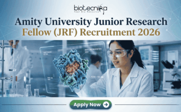 Amity University Junior Research Fellow (JRF) Recruitment 2026 | Apply Now Amity University Junior Research Fellow (JRF) Recruitment 2026 Apply Now. A featured image for a job posting titled "Amity University Junior Research Fellow (JRF) Recruitment 2026." At the top center is the Biotecnika logo. Below it, the main heading reads "Amity University Junior Research Fellow (JRF) Recruitment 2026" in a bold, professional font. The background features a high-tech, modern laboratory where a female researcher in a white lab coat and safety goggles is intensely focused on a glowing, 3D holographic molecular model representing drug research. The lab is clean and corporate, with various scientific equipment visible in soft focus. At the bottom center, there is a prominent green "Apply Now" button with a white arrow icon. The overall color palette is a professional mix of blue, white, and teal, designed to be eye-catching and authoritative.