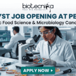 Analyst Job at PepsiCo BSc Food Science & Microbiology. A promotional banner from Biotecnika advertising an "ANALYST JOB OPENING AT PEPSICO for BSc Food Science & Microbiology Candidates". The visual features a female researcher in a lab coat and safety glasses using a compound microscope to examine colorful samples in a Petri dish. Laboratory equipment, test bottles with various food product liquids, and a male colleague working at a computer station are in the background. The Biotecnika logo is at the top, and a teal "APPLY NOW" button is at the bottom.