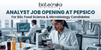 Analyst Job Opening at PepsiCo for BSc Food Science & Microbiology Candidates Analyst Job at PepsiCo BSc Food Science & Microbiology. A promotional banner from Biotecnika advertising an "ANALYST JOB OPENING AT PEPSICO for BSc Food Science & Microbiology Candidates". The visual features a female researcher in a lab coat and safety glasses using a compound microscope to examine colorful samples in a Petri dish. Laboratory equipment, test bottles with various food product liquids, and a male colleague working at a computer station are in the background. The Biotecnika logo is at the top, and a teal "APPLY NOW" button is at the bottom.