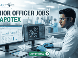 Apotex Hiring Junior Officers in Bangalore | Life Science Graduates Apply Now! Apotex Hiring Junior Officers in Bangalore Apply Now! A professional recruitment banner for "JUNIOR OFFICER JOBS AT APOTEX" featuring the Biotecnika logo at the top left. The image depicts a young male pharmaceutical professional in a white lab coat and blue gloves, meticulously monitoring data on dual computer screens. One screen displays analytical charts and graphs, while the other shows a 3D molecular structure. In the background, a sterile pharmaceutical production line with stainless steel machinery is visible through a large glass partition. On the right side, vertical teal icons highlight key roles: "QC QA," "Data Analysis," "Sterile Production," "Sterile vial," and "Ladder chart." A prominent green "APPLY NOW" button with a white arrow is centered at the bottom.