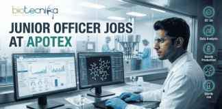 Apotex Hiring Junior Officers in Bangalore | Life Science Graduates Apply Now! Apotex Hiring Junior Officers in Bangalore Apply Now! A professional recruitment banner for "JUNIOR OFFICER JOBS AT APOTEX" featuring the Biotecnika logo at the top left. The image depicts a young male pharmaceutical professional in a white lab coat and blue gloves, meticulously monitoring data on dual computer screens. One screen displays analytical charts and graphs, while the other shows a 3D molecular structure. In the background, a sterile pharmaceutical production line with stainless steel machinery is visible through a large glass partition. On the right side, vertical teal icons highlight key roles: "QC QA," "Data Analysis," "Sterile Production," "Sterile vial," and "Ladder chart." A prominent green "APPLY NOW" button with a white arrow is centered at the bottom.