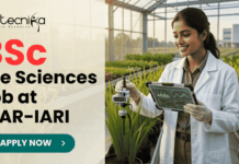 BSc Life Sciences Job Opportunity at ICAR-IARI Work on DBT Funded Project. A promotional image banner from biotecnika for a "BSc Life Sciences Job at ICAR-IARI". It features a photograph of a smiling female researcher in a white lab coat, holding a data tablet and adjusting a scientific sensor on a growing plant in a modern, sunlit greenhouse. A centrifuge and test tubes on a cart are to her side. The biotecnika logo is at the top left, and a green "APPLY NOW" button with an arrow is at the bottom center.