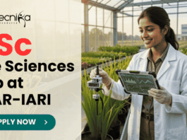 BSc Life Sciences Job Opportunity at ICAR-IARI Work on DBT Funded Project. A promotional image banner from biotecnika for a "BSc Life Sciences Job at ICAR-IARI". It features a photograph of a smiling female researcher in a white lab coat, holding a data tablet and adjusting a scientific sensor on a growing plant in a modern, sunlit greenhouse. A centrifuge and test tubes on a cart are to her side. The biotecnika logo is at the top left, and a green "APPLY NOW" button with an arrow is at the bottom center.